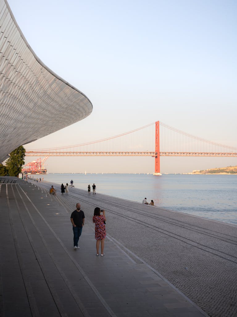 Scenic view of people walking near the Tagus River with the 25 de Abril Bridge in Lisbon, Portugal for blog post of investing in Portugal